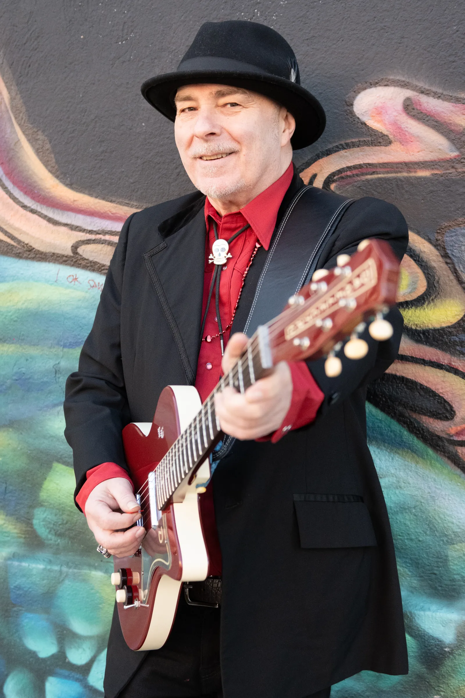 Tim Gibbons laughing with his guitar in front of a mural
