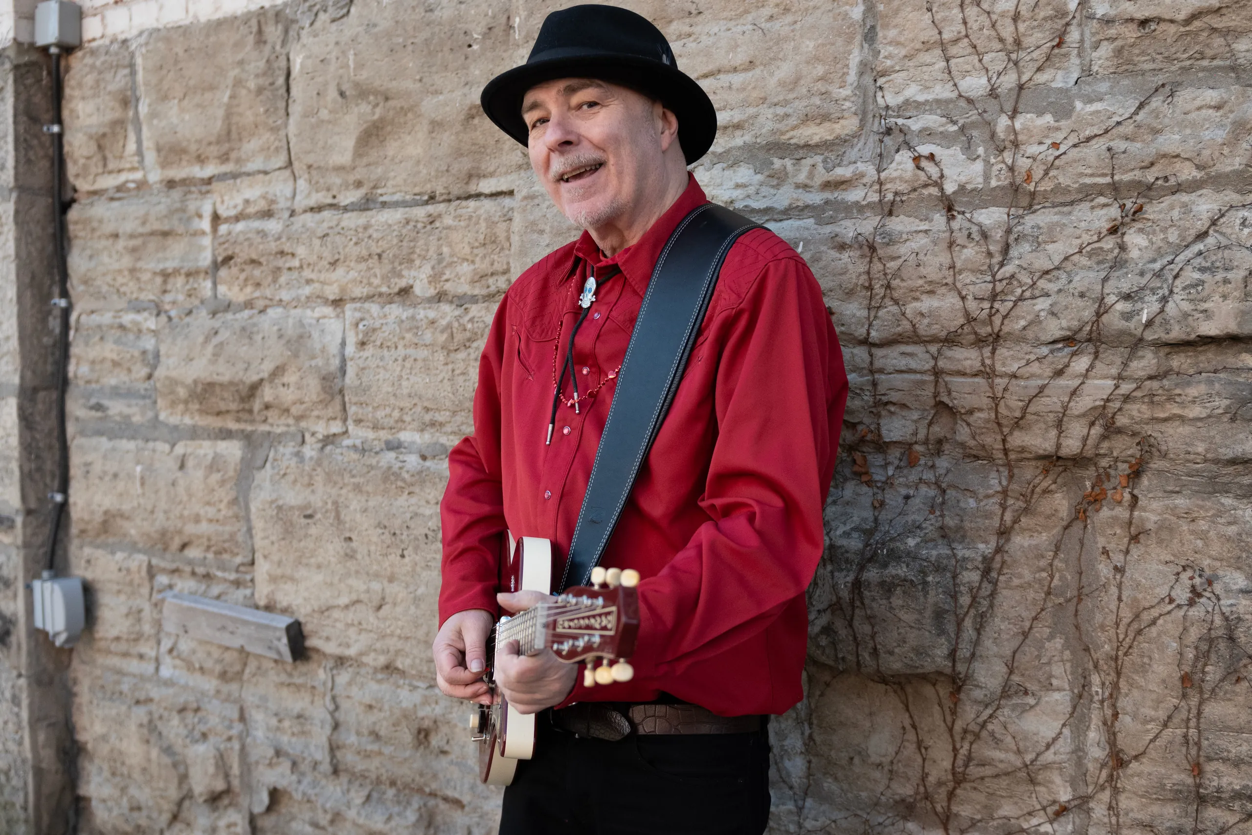 Tim Gibbons with his guitar against a Hamilton stone wall
