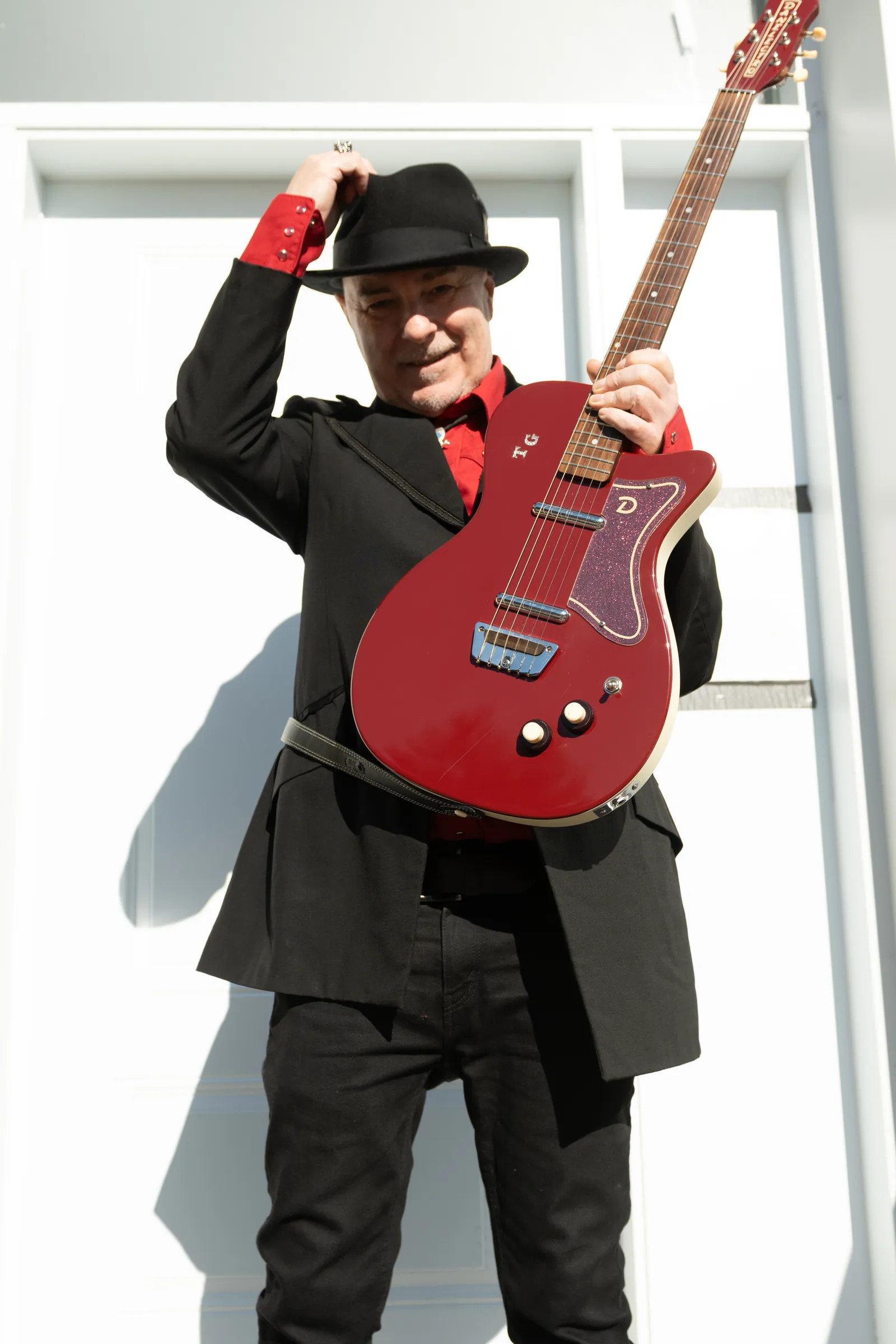 Tim Gibbons tipping his hat with a red guitar